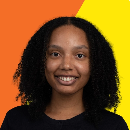 A young woman of color, smiling, wearing a black shirt on a bright orange and yellow background.